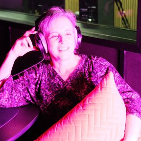 Pink hue podcast guest - phot of white middle aged woman in headphones holding cushion