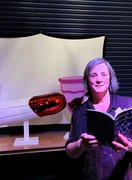 Vagina Museum edited anthology reading white older woman on stage reading - with glittery tampon and mooncup behind